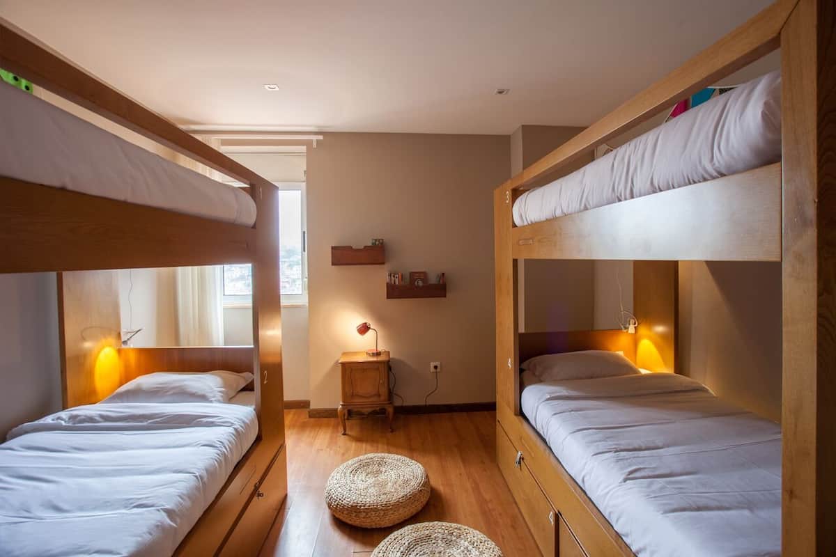 A room with two bunk beds, a small wooden nightstand, a lamp, and a woven mat on the floor.