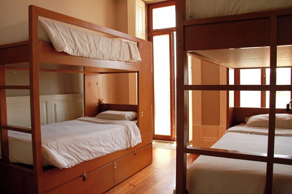 A room with two bunk beds, wooden flooring, and a window providing natural light.