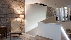 Un interior moderno con una pared de piedra, una escalera blanca y una silla de madera.