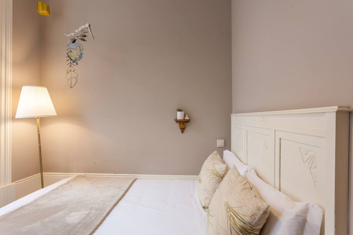 A bedroom with a bed, a lamp, a wall-mounted light, and a decorative hanging.