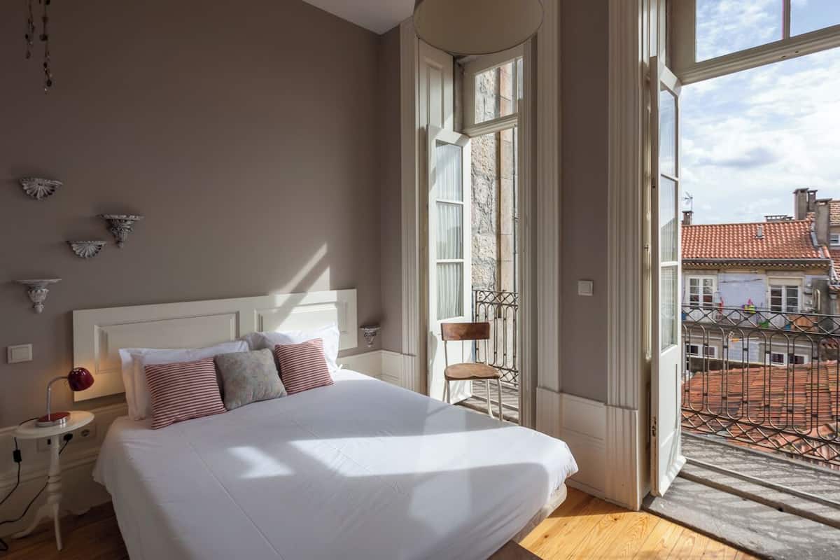 A bedroom with a large bed, a nightstand, a chair, and a window with a view of buildings.