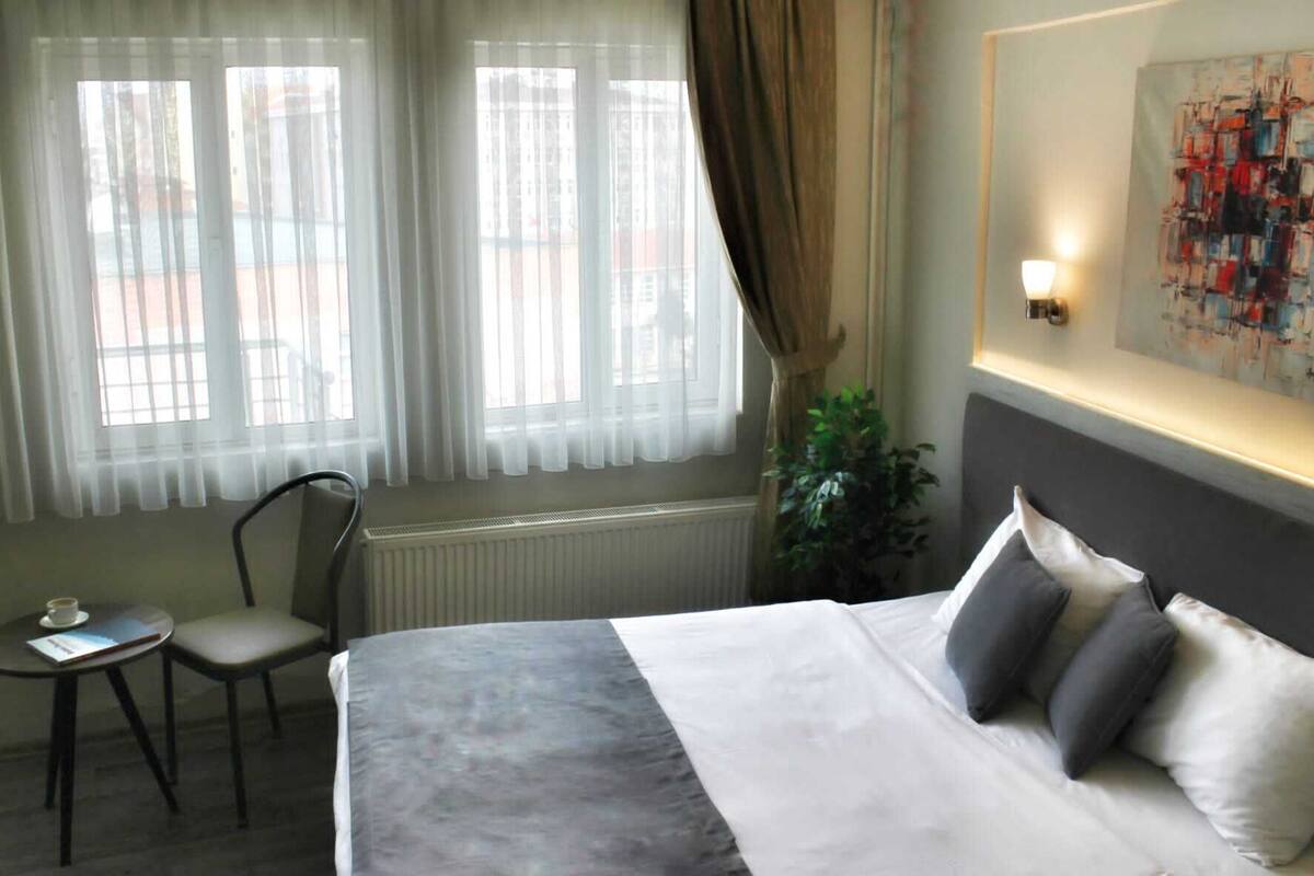 A hotel room with a bed, a chair, a small table, and a window with curtains.