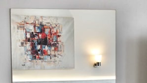 Un dormitorio moderno de hotel con una cama, un cuadro abstracto colgado en la pared, una lámpara de noche, una revista y una taza de café sobre una mesita.