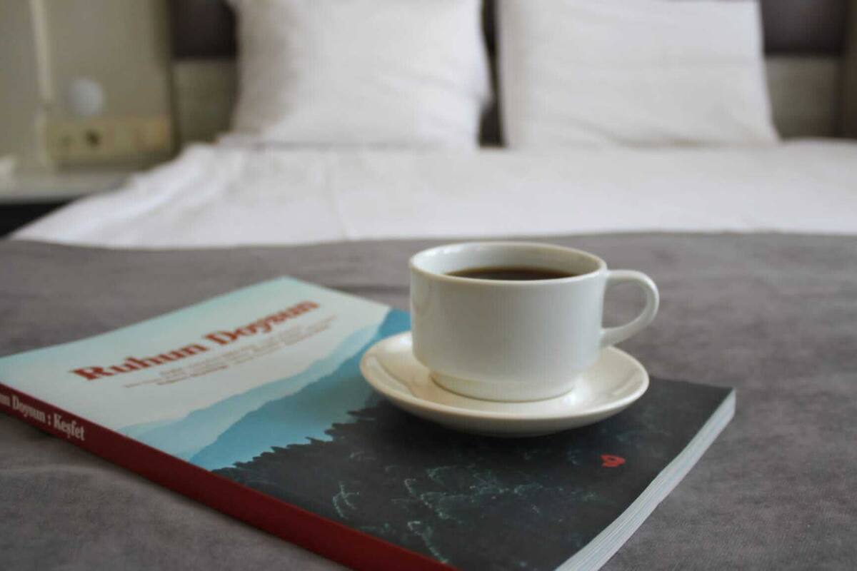 A bed with a white pillow and a cup of coffee on a saucer. A book titled "Ruham Doyman" is placed on the bed.