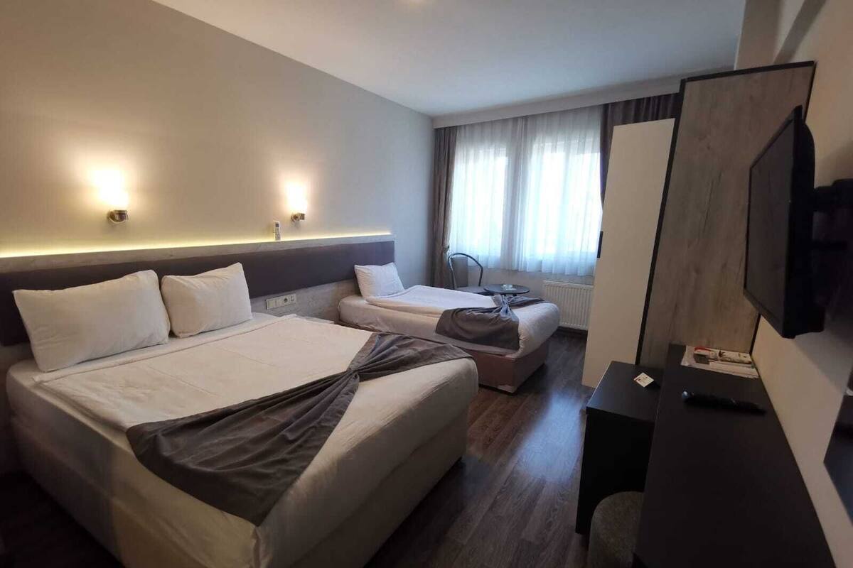 A hotel room with two beds, a desk, a chair, a TV, and a window with curtains.
