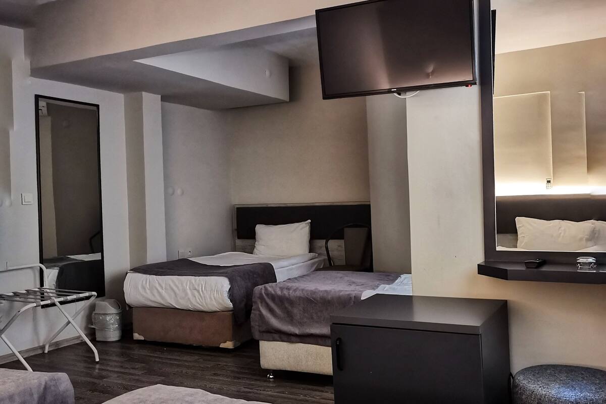 A hotel room with two beds, a flat-screen TV mounted on the wall, a small table, and a trash bin.