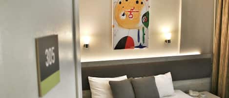 A hotel room with a bed, pillows, a nightstand, a lamp, and a wall art piece.