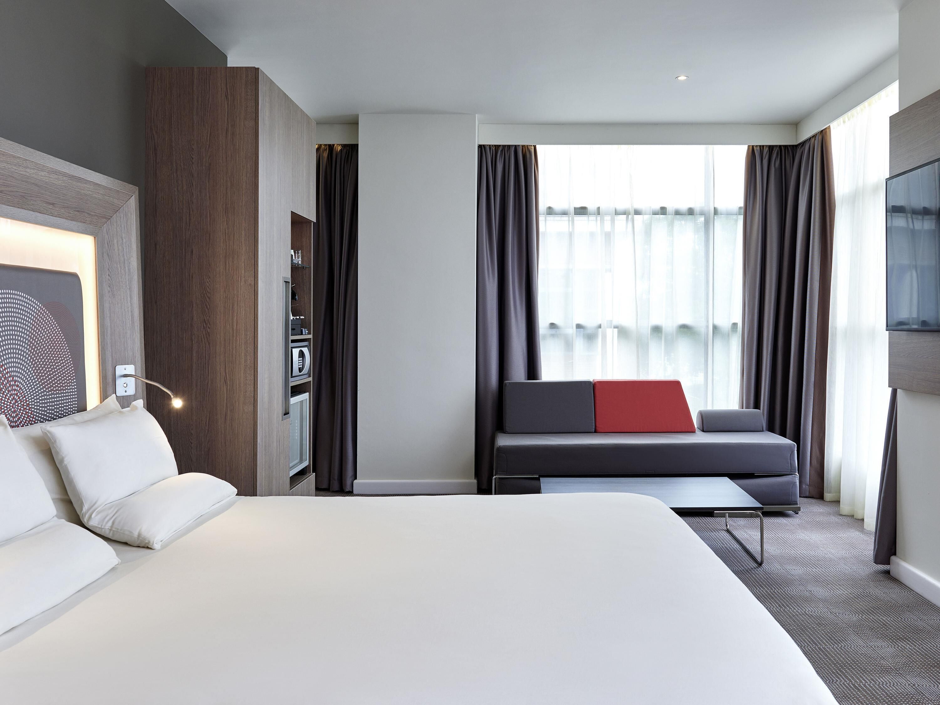Une chambre d’hôtel avec un grand lit, un canapé avec un coussin rouge, un bureau et une télévision.
