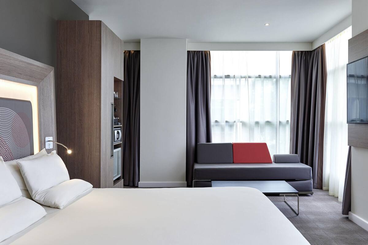 Une chambre d’hôtel avec un grand lit, un canapé avec un coussin rouge, un bureau et une télévision.