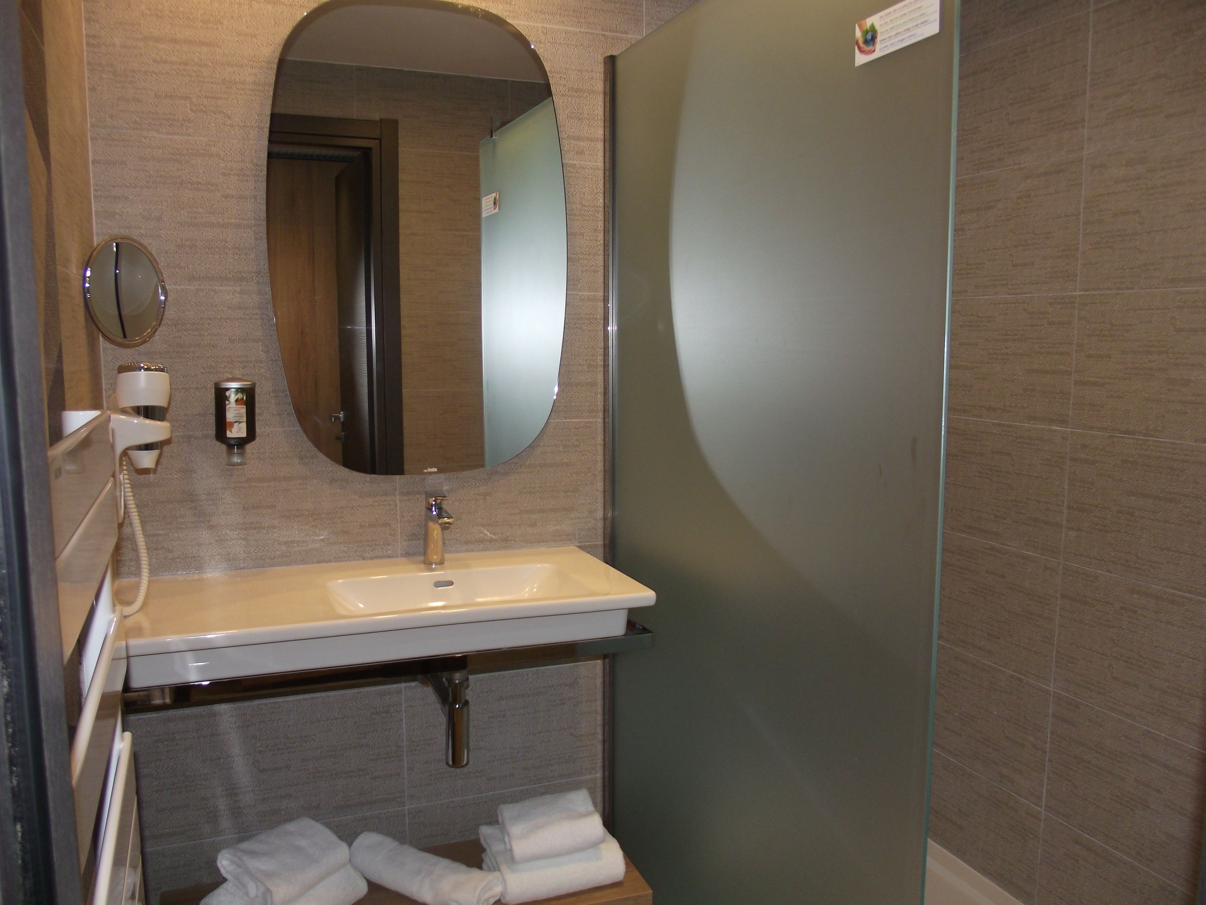 A bathroom with a sink, mirror, towel rack, and shower stall.