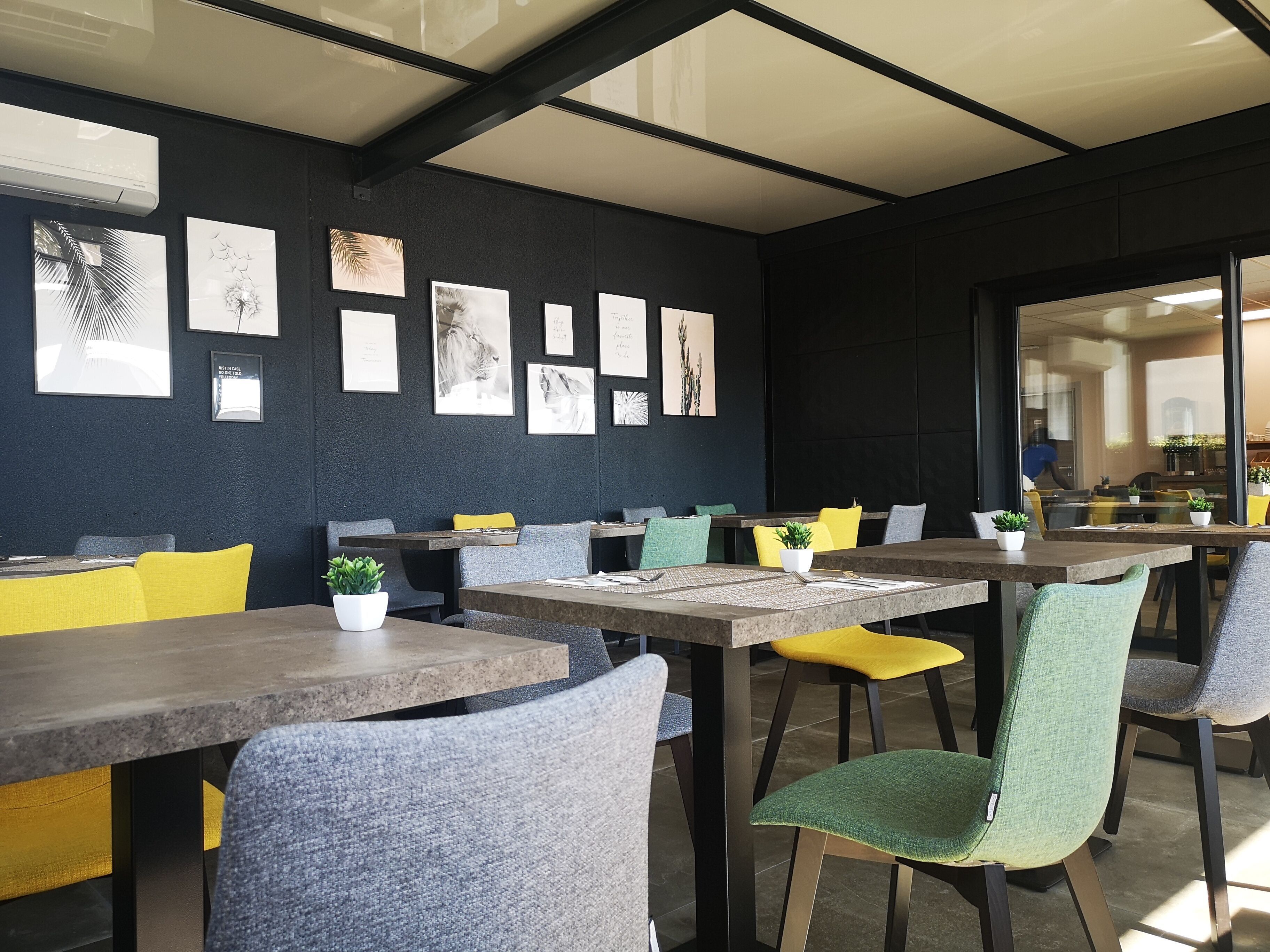 A modern dining area with tables and chairs, artwork on the walls, and a view of the kitchen through a glass door.