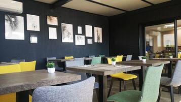 Un comedor moderno con mesas y sillas, obras de arte en las paredes y vista a la cocina a través de una puerta de vidrio.