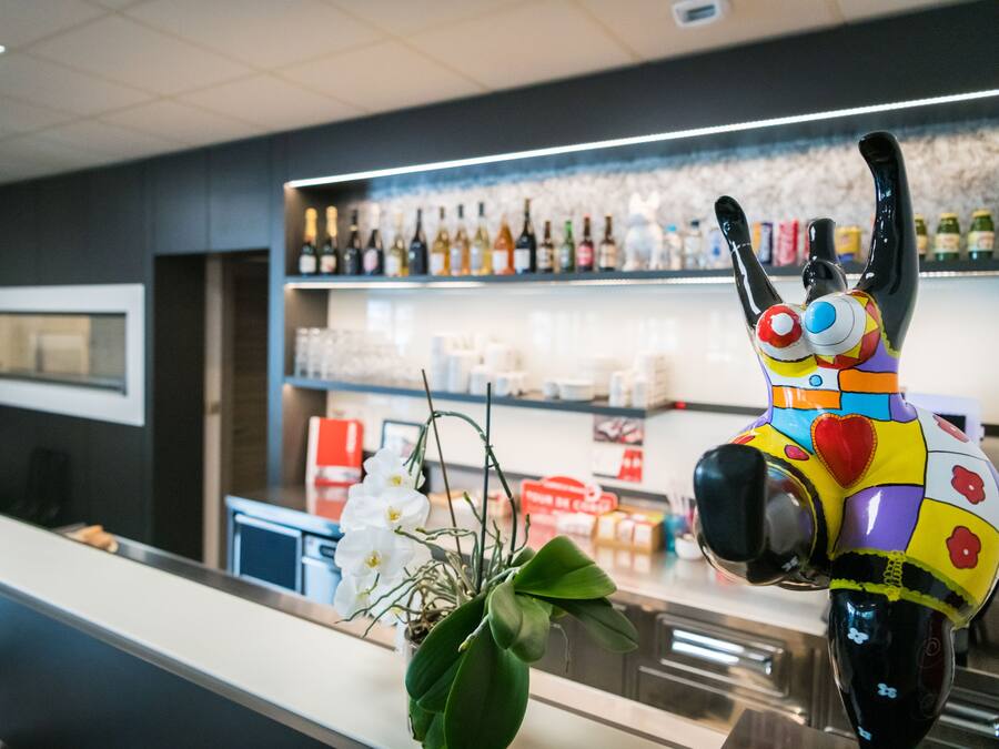 Zona de bar con una estatua colorida, estantes llenos de botellas y una barra.