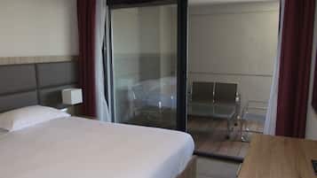 Habitación de hotel con cama, escritorio, silla y puerta corrediza de vidrio que da a un balcón.