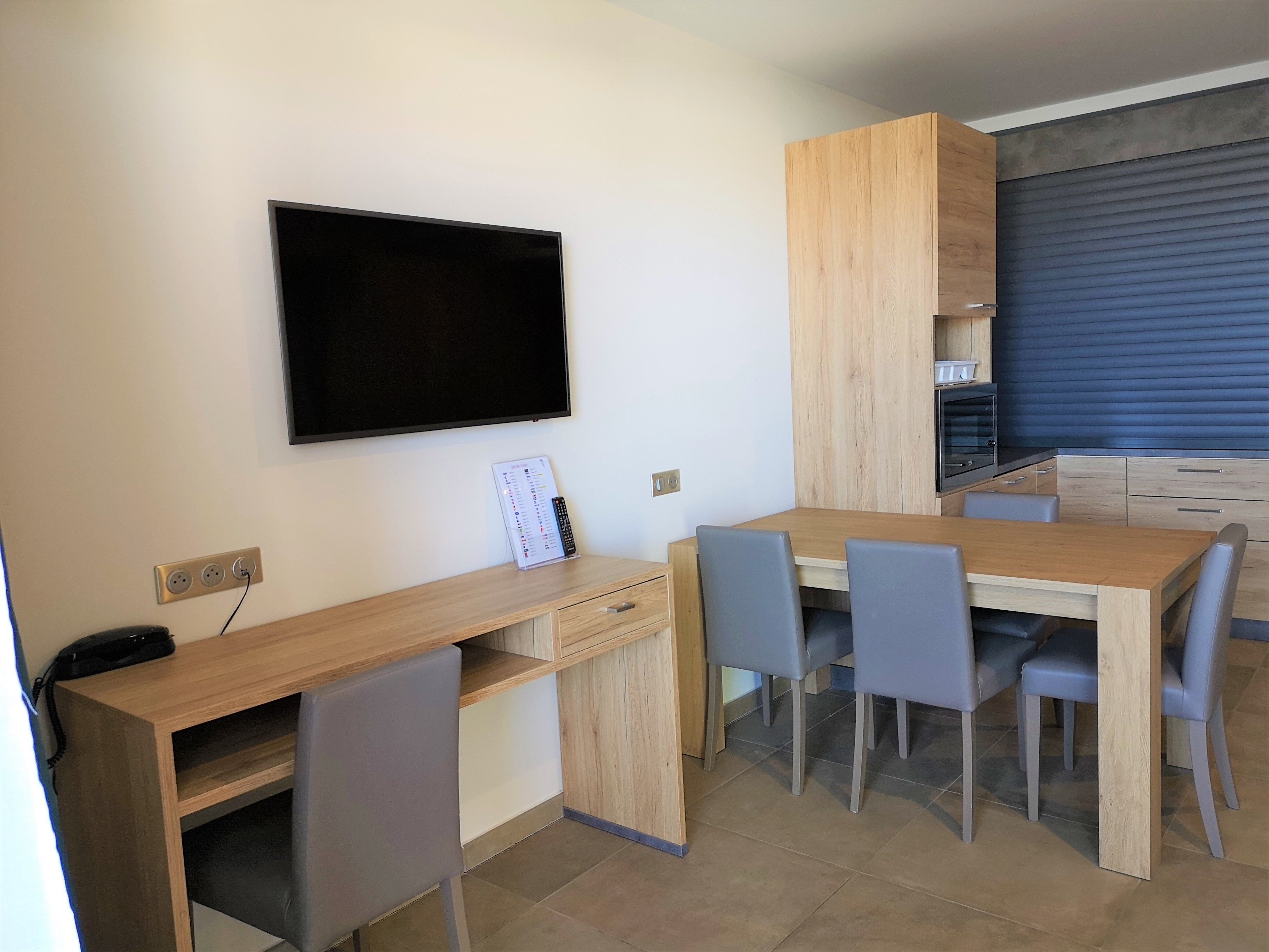 Cocina compacta con horno empotrado, una mesa de comedor con sillas y un televisor de pantalla plana montado en la pared.