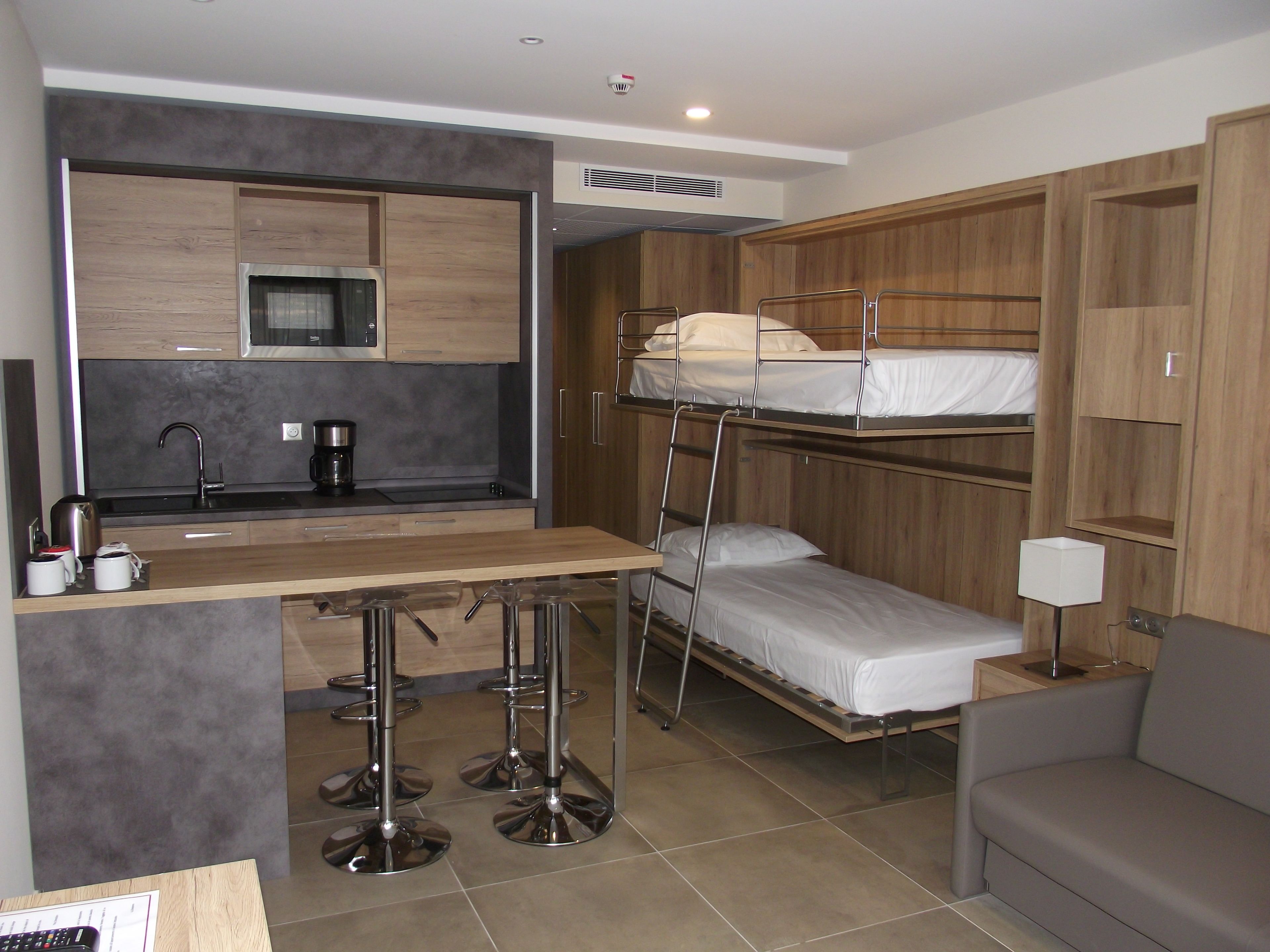 Ein kompaktes Hotelzimmer mit Küchenzeile, Etagenbetten, einer kleinen Couch und einer Bar mit Barhocker.
