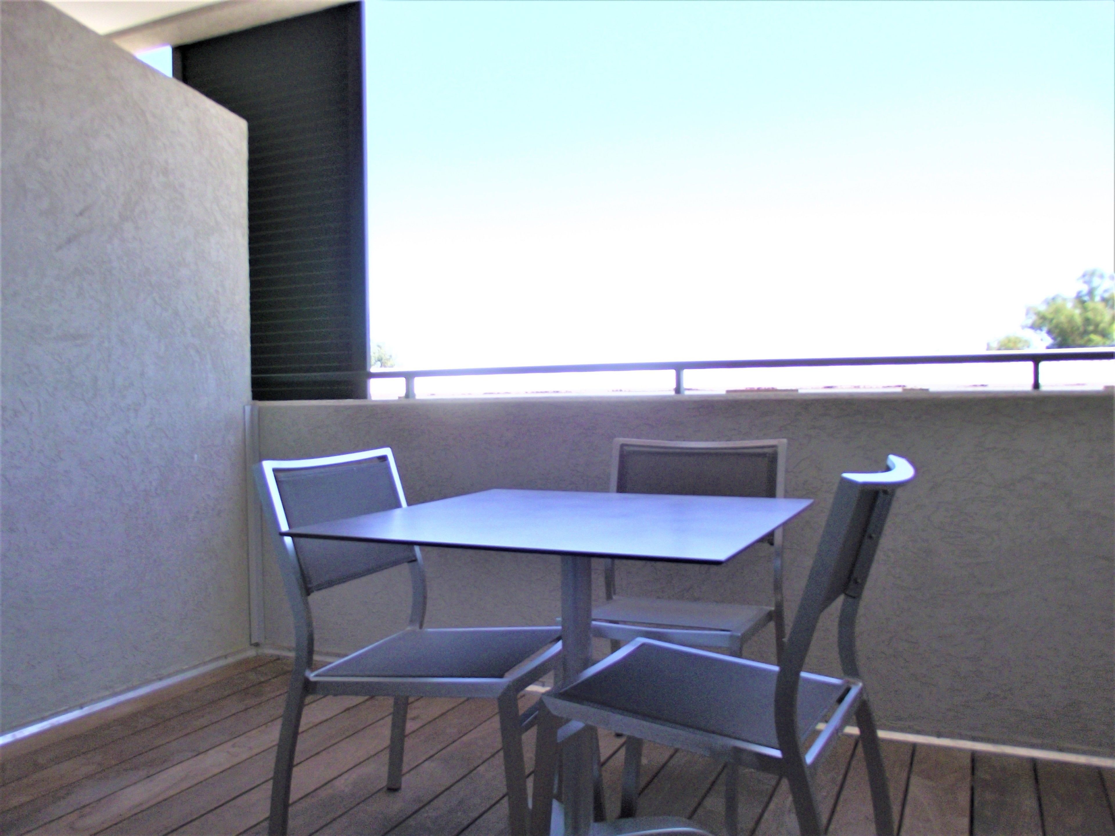 A balcony with a table and two chairs, a view of the sky, and a building in the background.