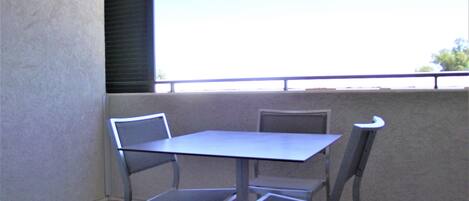 A balcony with a table and two chairs, a view of the sky, and a building in the background.