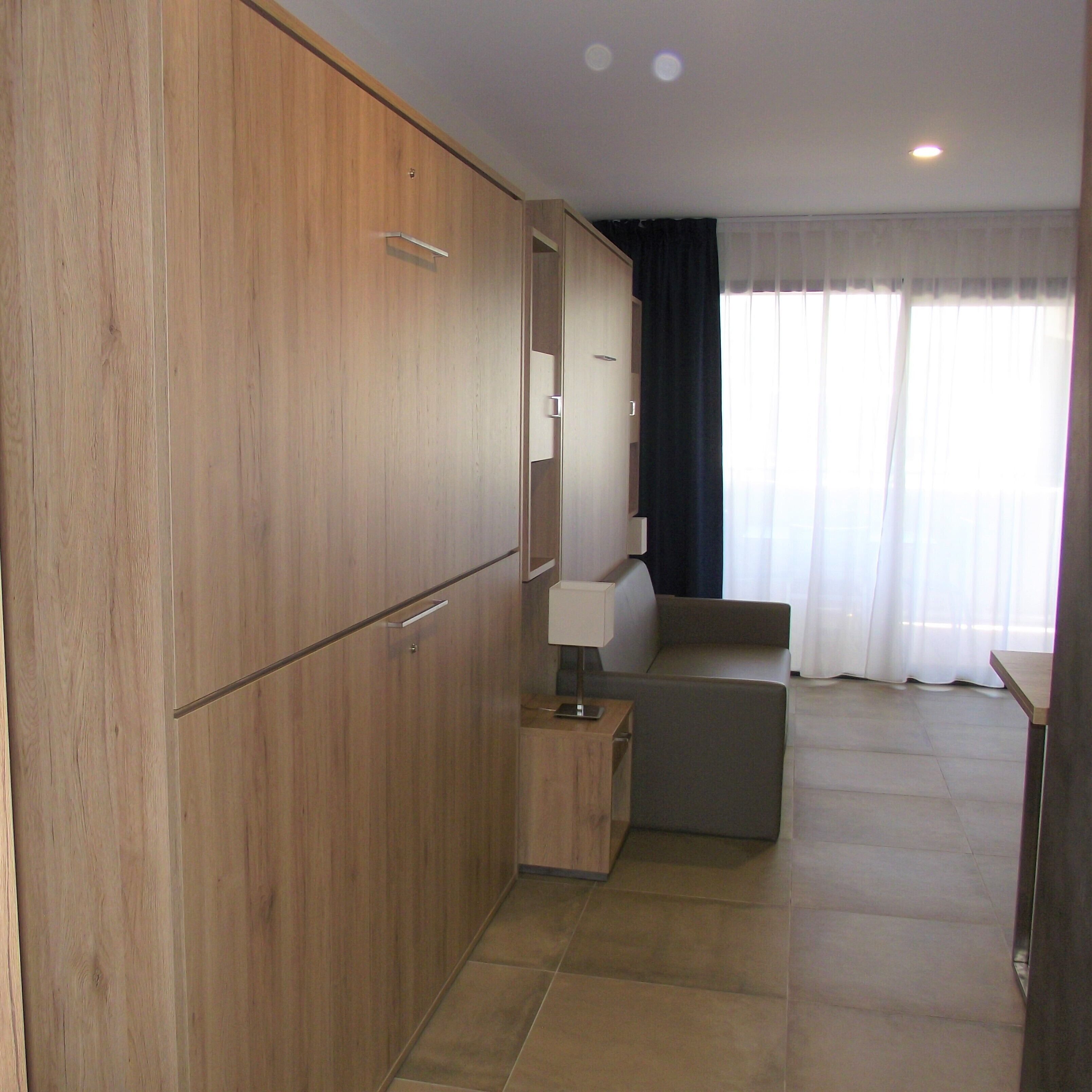 A modern room with wooden wardrobes, a small table, a sofa, and a window with curtains.