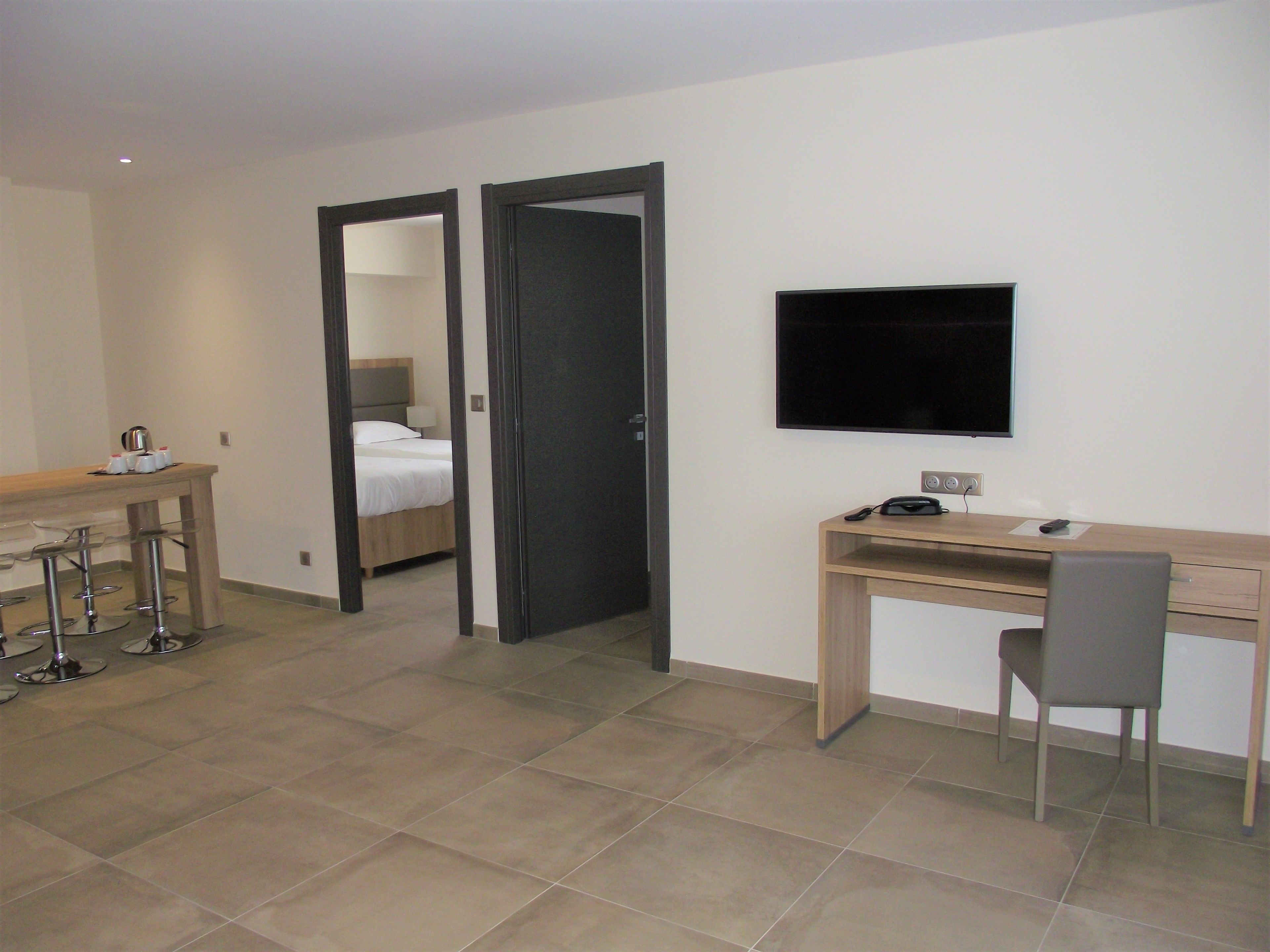 A hotel room with a bed, a desk with a chair, a TV, and a minibar.
