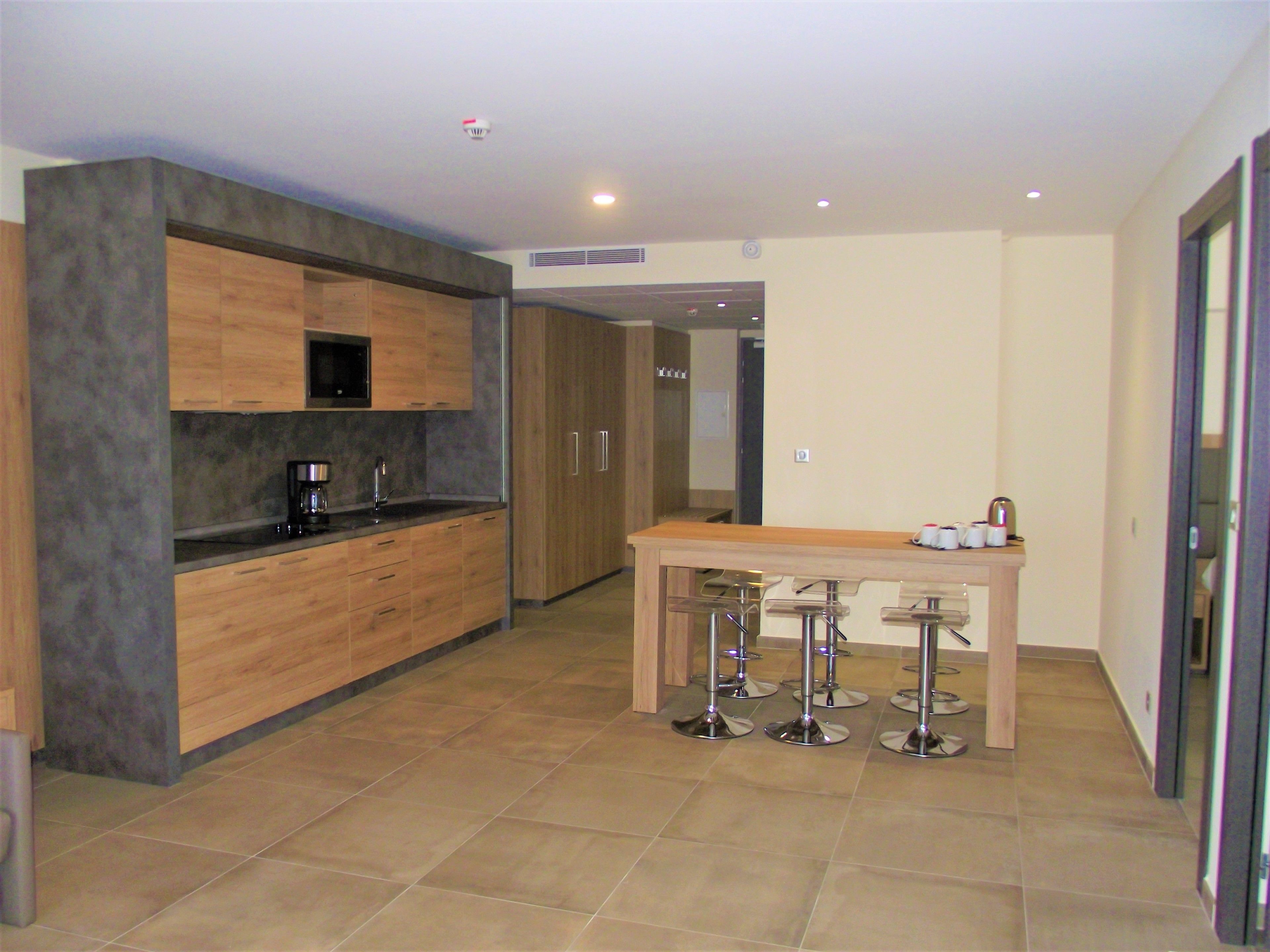 A modern kitchen with wooden cabinets, a coffee maker, and a bar area with stools.