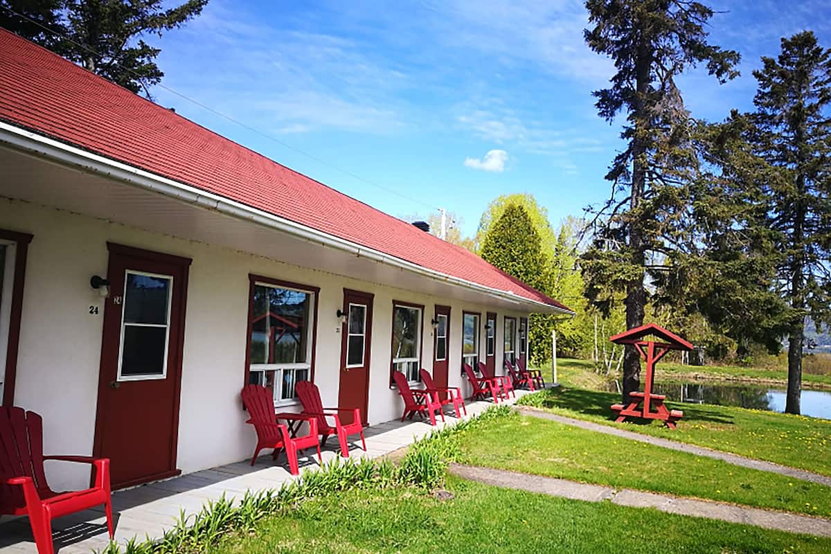 A two-story building with a red roof and white walls, featuring a row of red chairs outside and a small red gazebo.