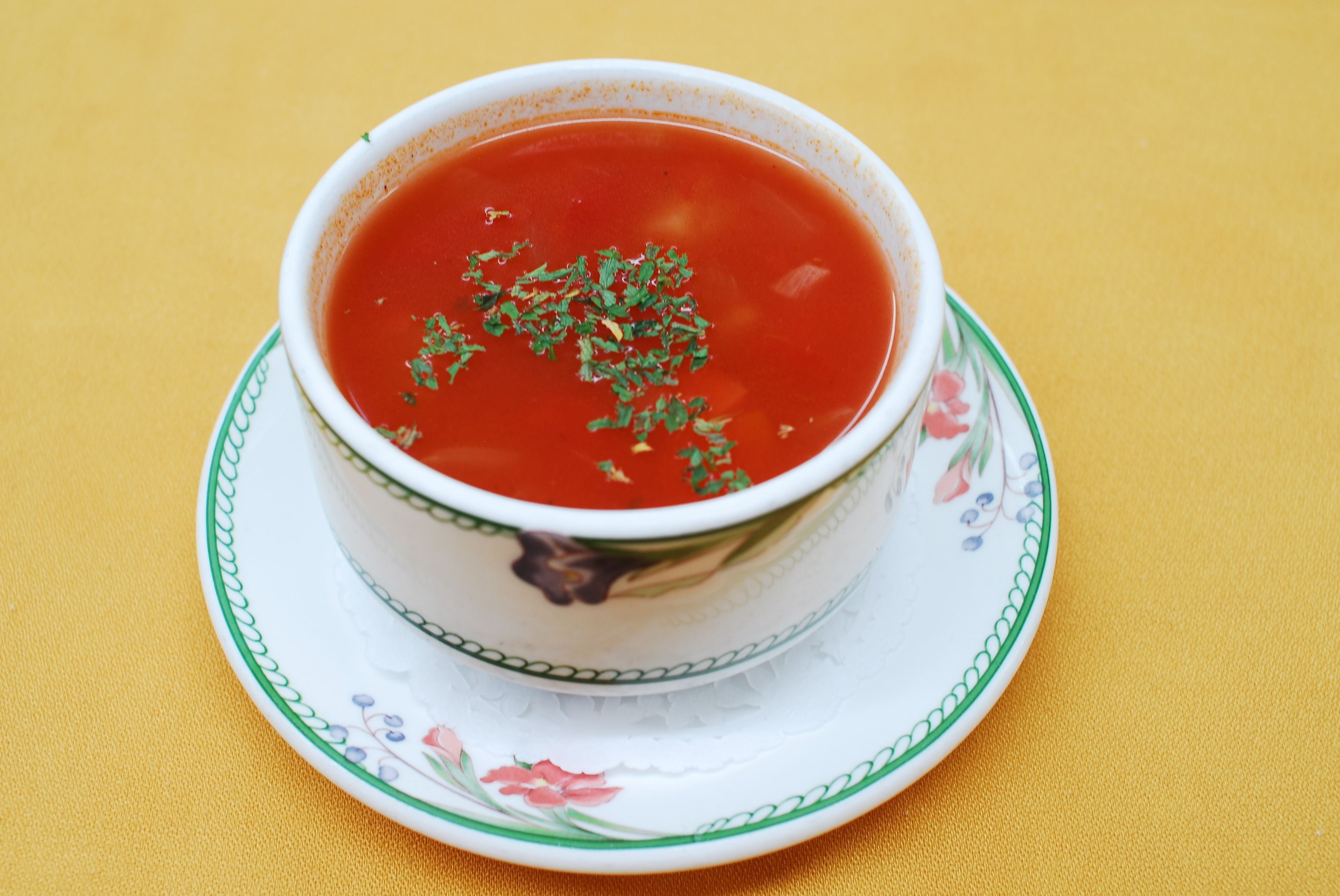 A bowl of soup on a floral-patterned saucer.