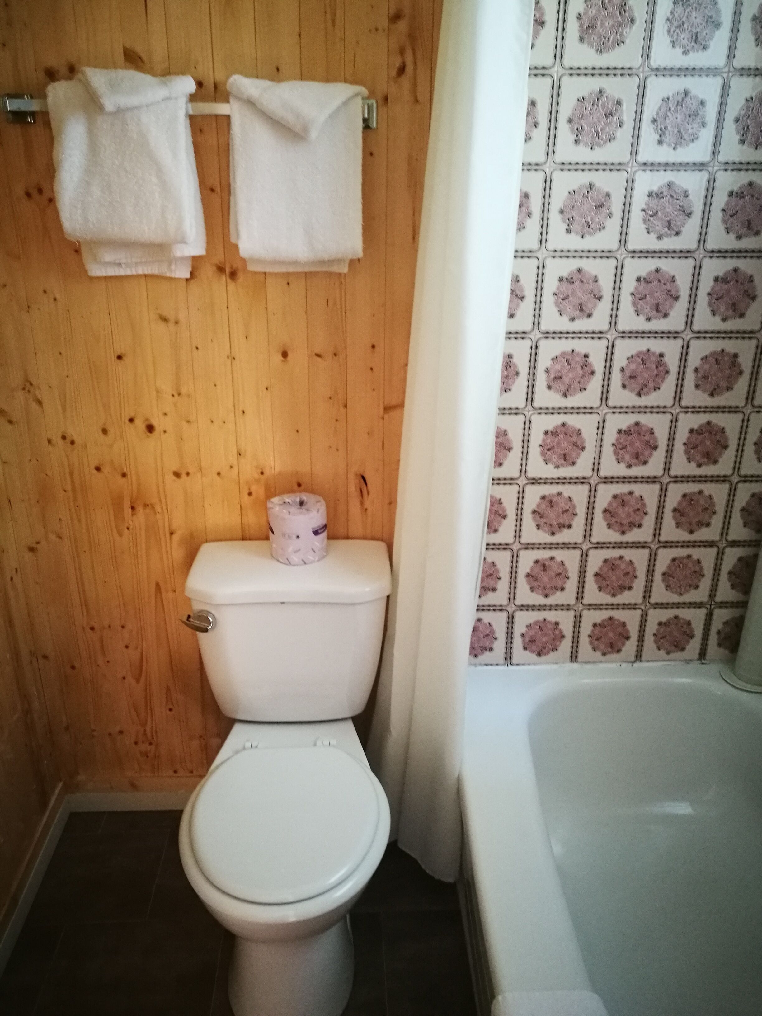 Een badkamer met een houten wand, toilet, bad en douchegordijn.