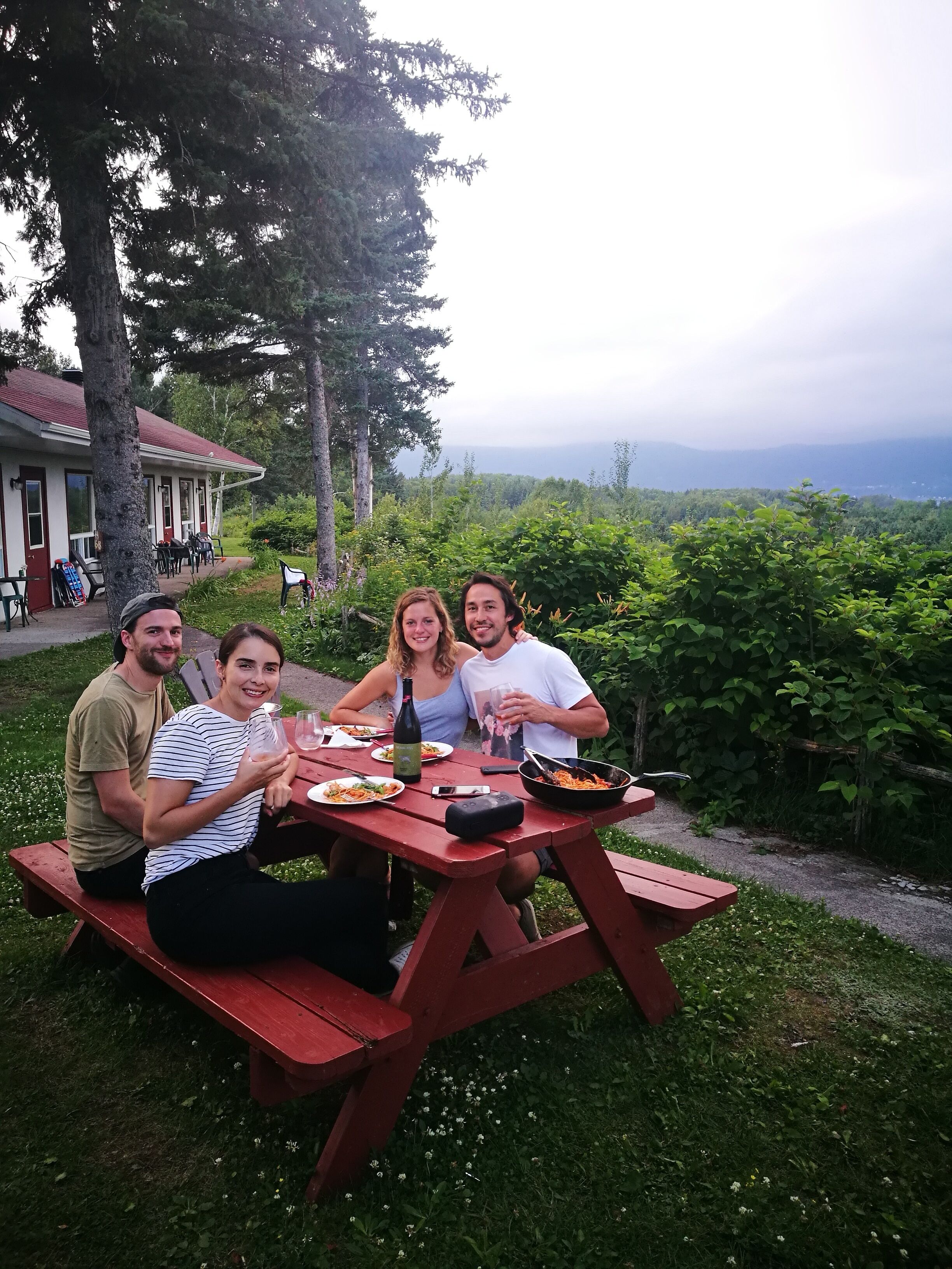 A group of people dining at a red picnic table outdoors with a scenic view in the background.