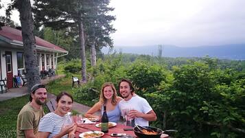A group of people dining at a red picnic table outdoors with a scenic view in the background.