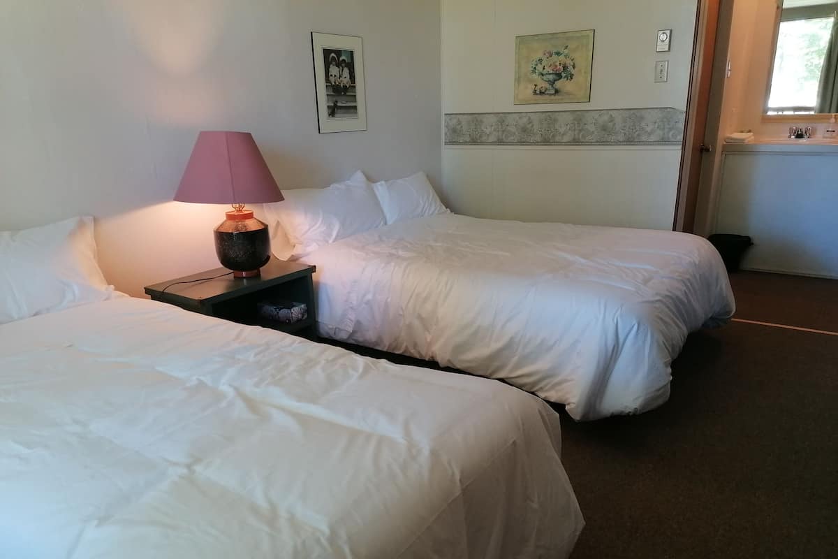 A hotel room with two beds, a nightstand with a lamp, a picture on the wall, and a window with curtains.