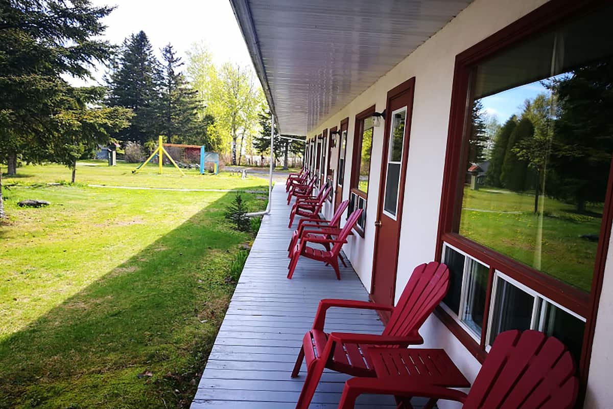 A covered porch with red Adirondack chairs, a grassy yard, and a playground in the background.