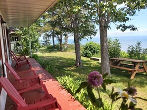 A covered outdoor seating area with red chairs and a picnic table, overlooking a grassy landscape and a body of water.