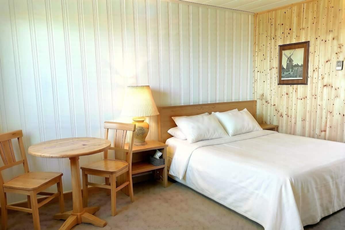 A hotel room with a bed, a round wooden table with chairs, a lamp, and a wall-mounted picture.