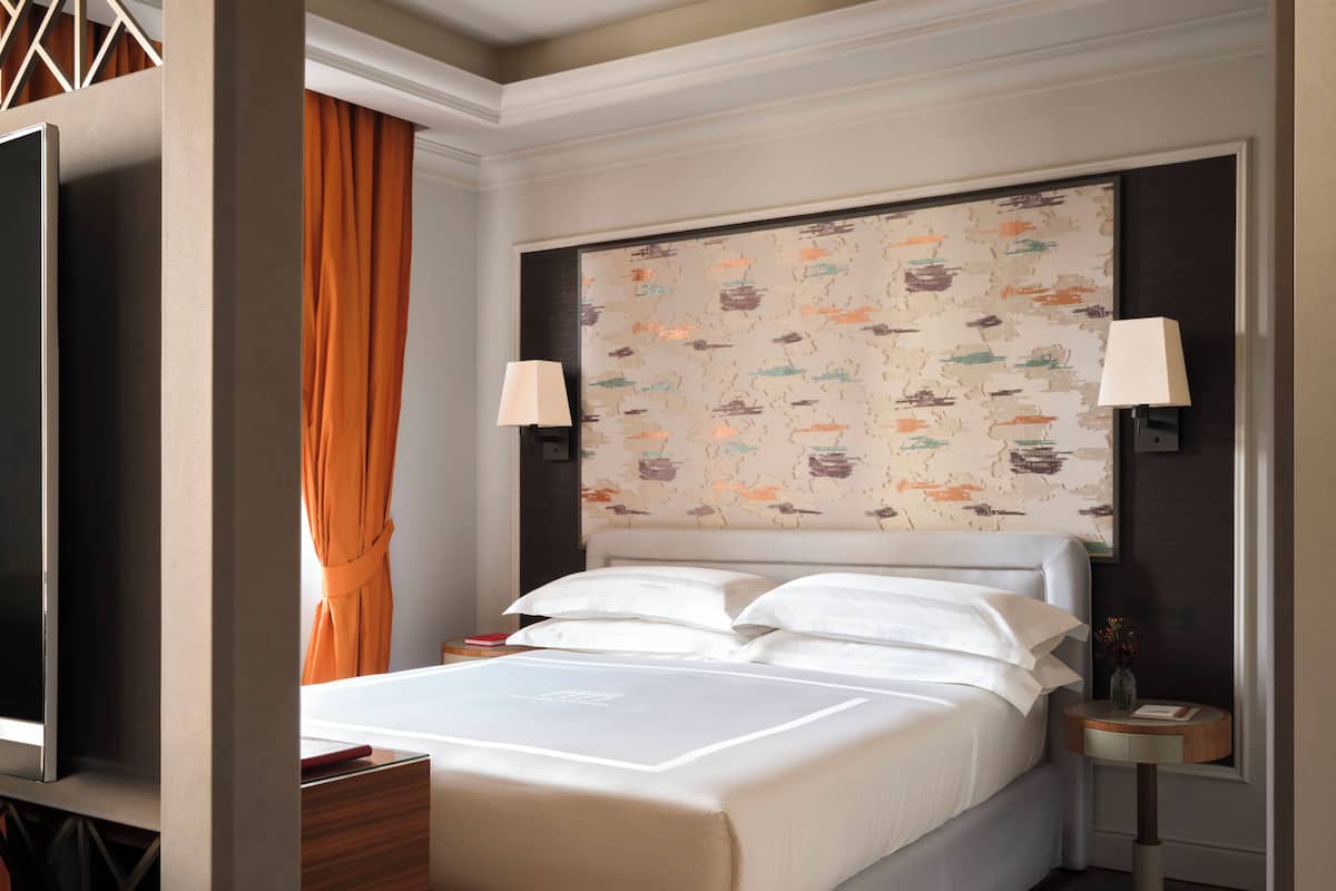 A hotel room with a large bed, two bedside lamps, a flat-screen TV, and a small table with a book and a vase.