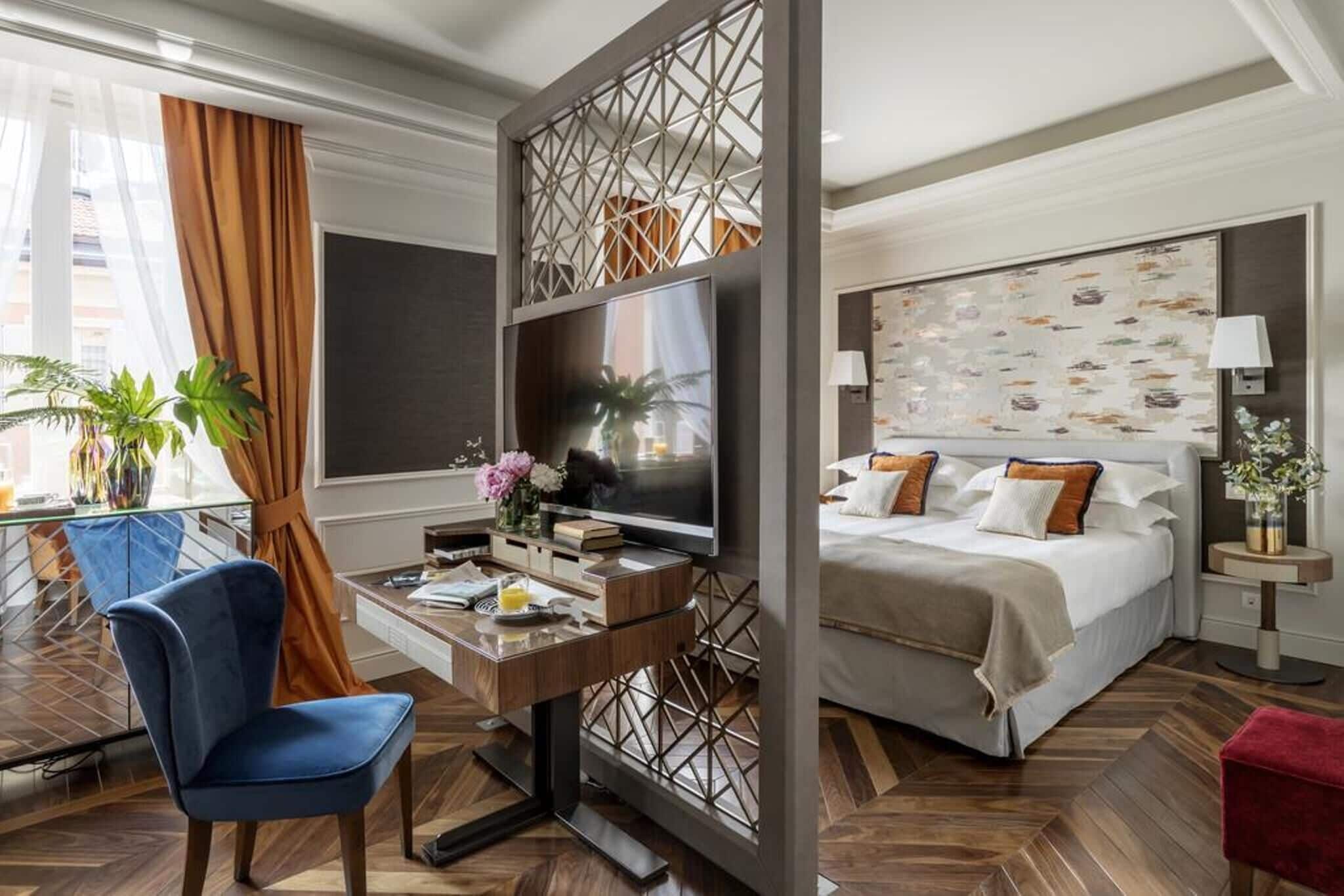 A hotel room with a desk, chair, TV, bed, and decorative wall panel.