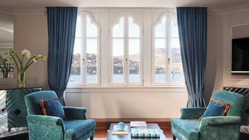 Un salon avec deux fauteuils turquoise, une table basse et une vue sur un lac, visible à travers des fenêtres en arc de cercle.