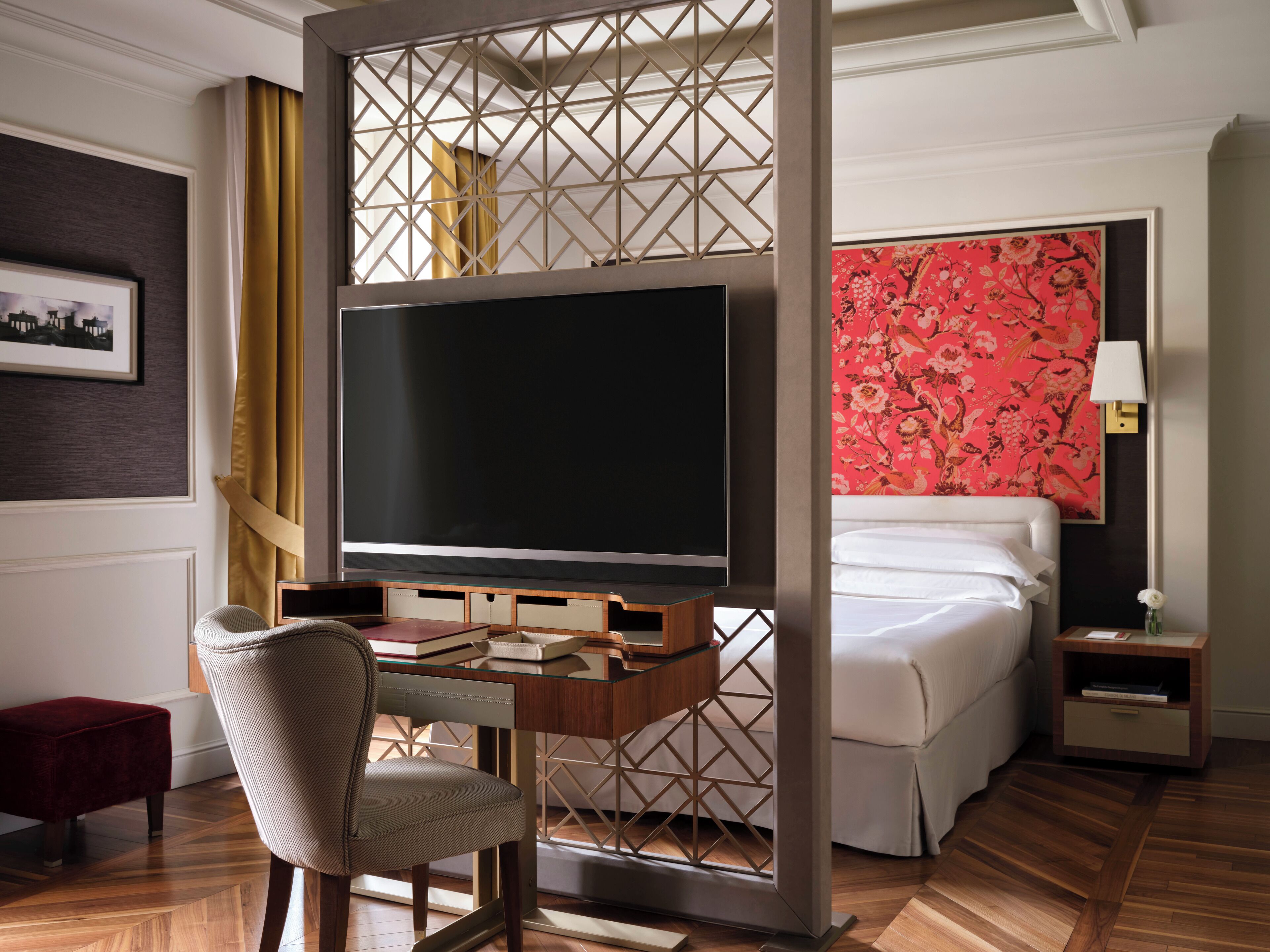 Habitación de hotel con una cama grande, un escritorio con televisor, una silla y una mesita de noche con lámpara.