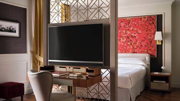 Habitación de hotel con una cama grande, un escritorio con televisor, una silla y una mesita de noche con lámpara.