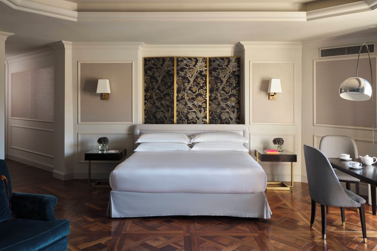 A hotel room with a large bed, two bedside tables, a chair, a desk, and a decorative wall panel.