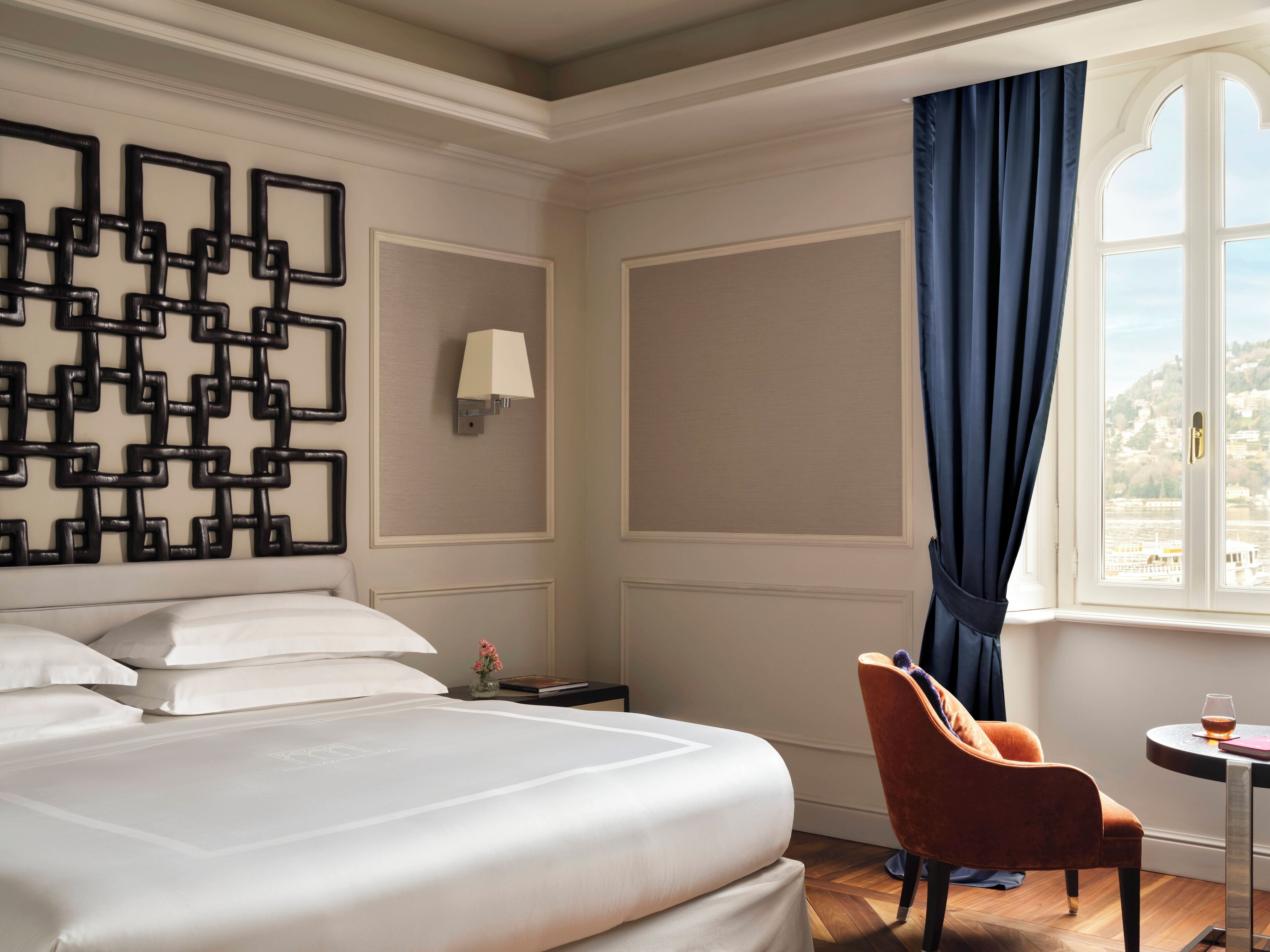 A hotel room with a large bed, a chair, a small table with a glass, and a window with curtains.