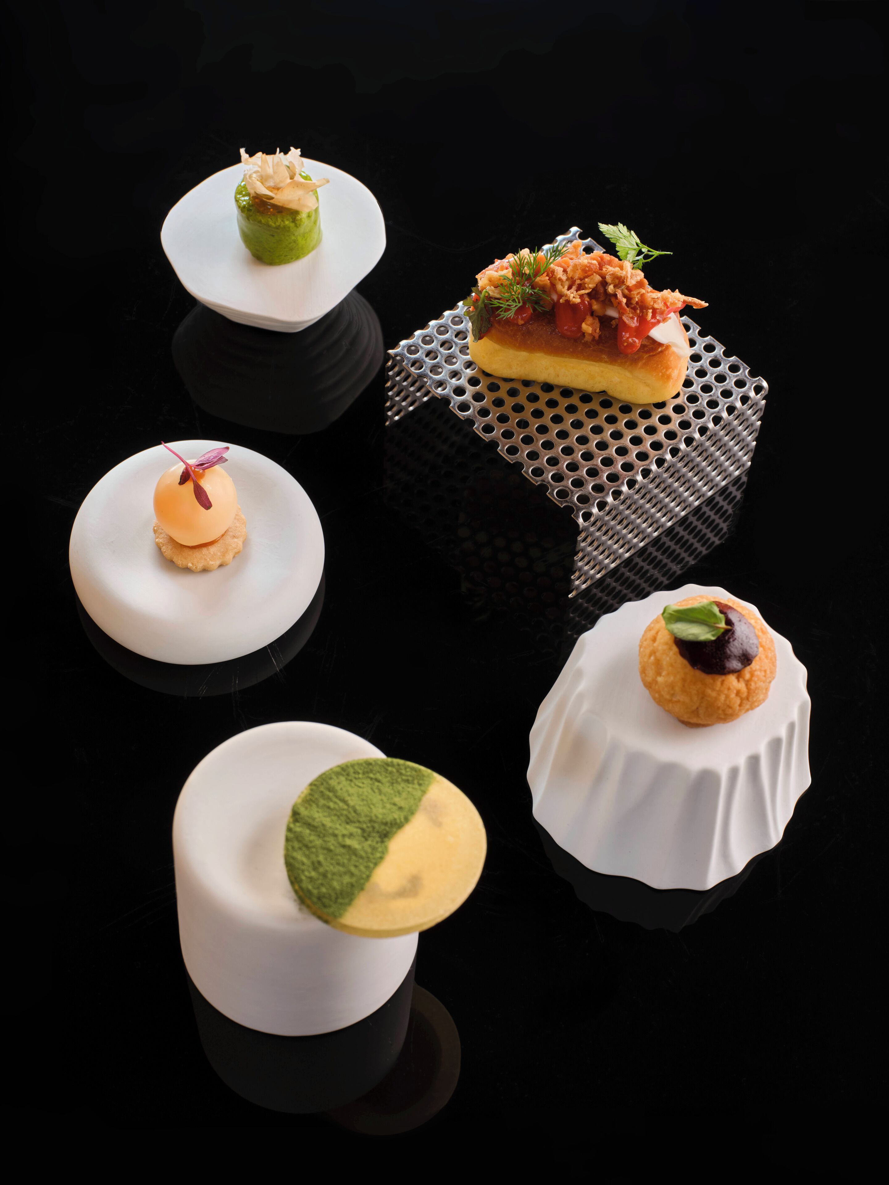 A variety of dessert presentations on white plates with a black background.