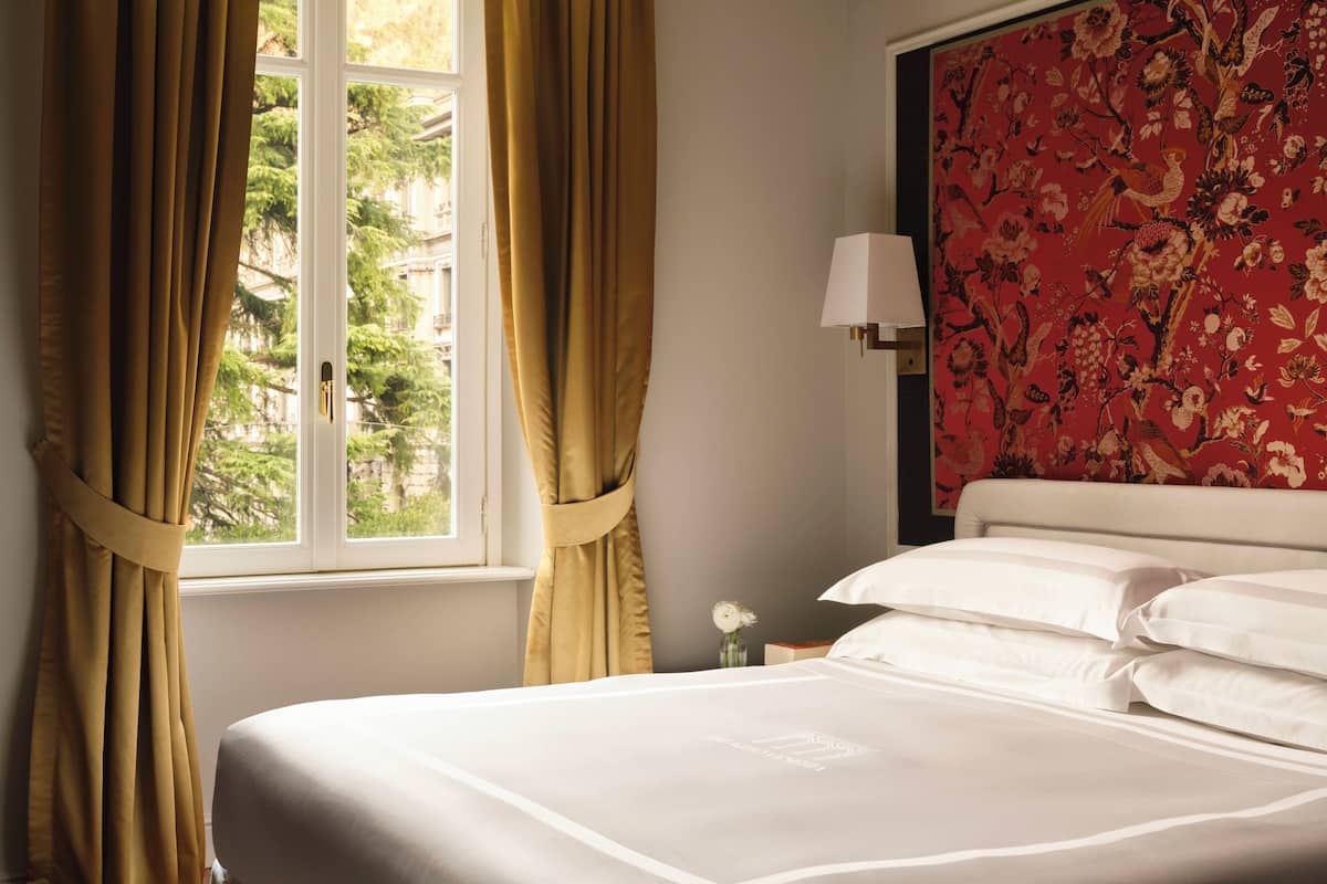 A hotel room with a bed, curtains, a window, and a floral wallpaper.