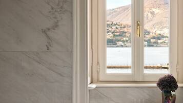 A bathroom with a large bathtub, a marble wall, and a window with a view of a mountainous landscape.