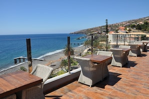Una terrazza con mobili in vimini che si affaccia su una spiaggia e l'oceano, con edifici sullo sfondo.