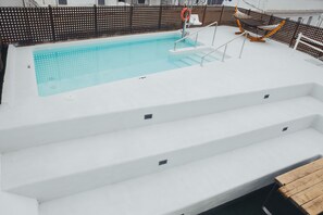En pool med trappsteg som leder ner i vattnet, omgiven av ett staket och en hängmatta.