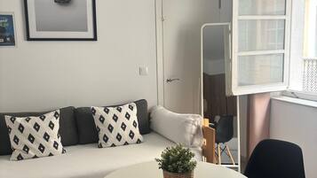 Una sala de estar moderna con un sofá, una mesa redonda con sillas, una planta en maceta y un cuadro en la pared.