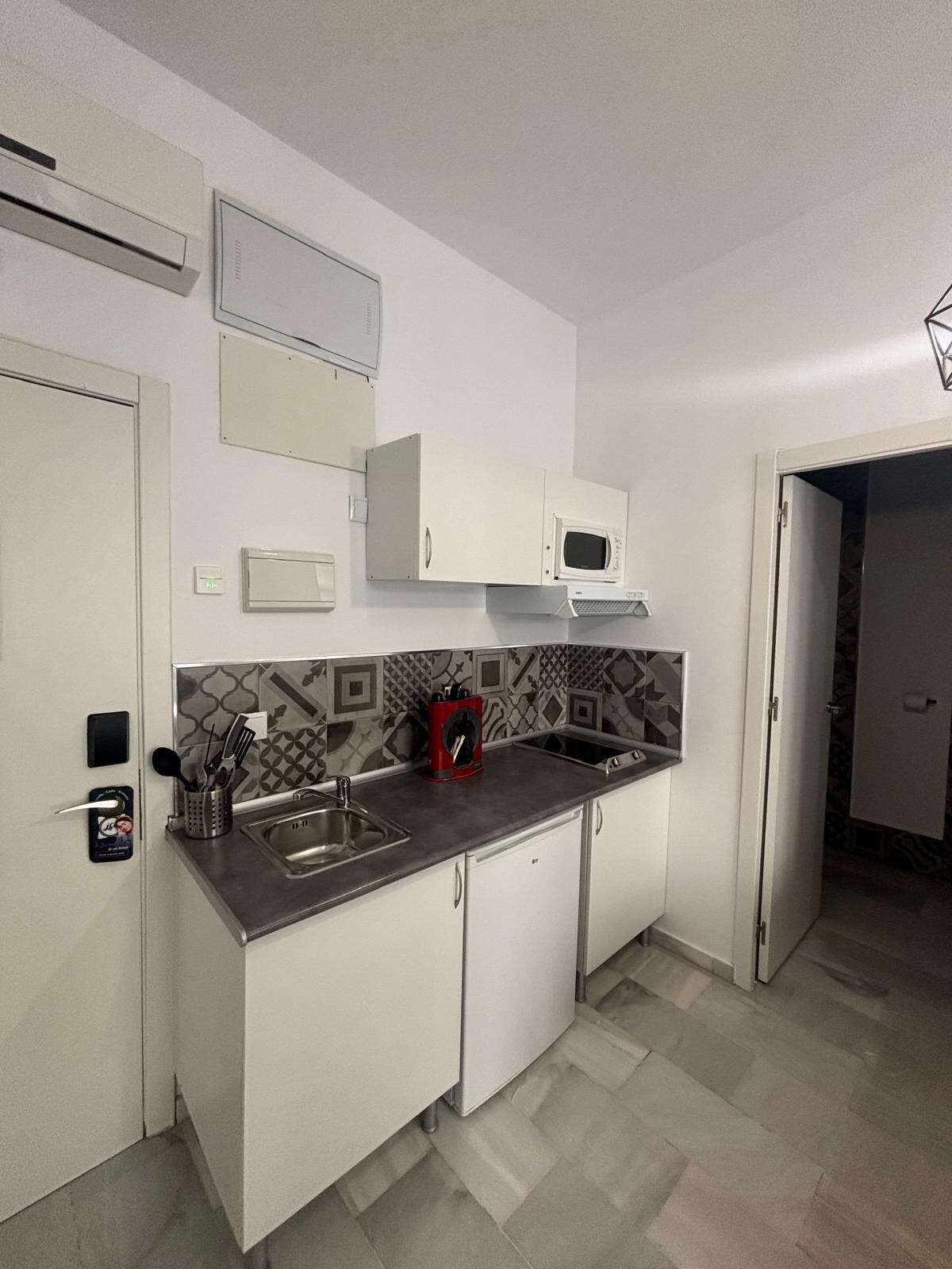 Una cocina pequeña con armarios blancos, microondas, pileta y salpicadero decorado.