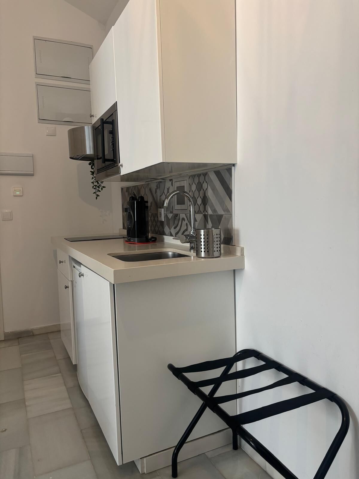 A compact kitchen with white cabinetry, a stainless steel microwave, a coffee machine, and a sink.