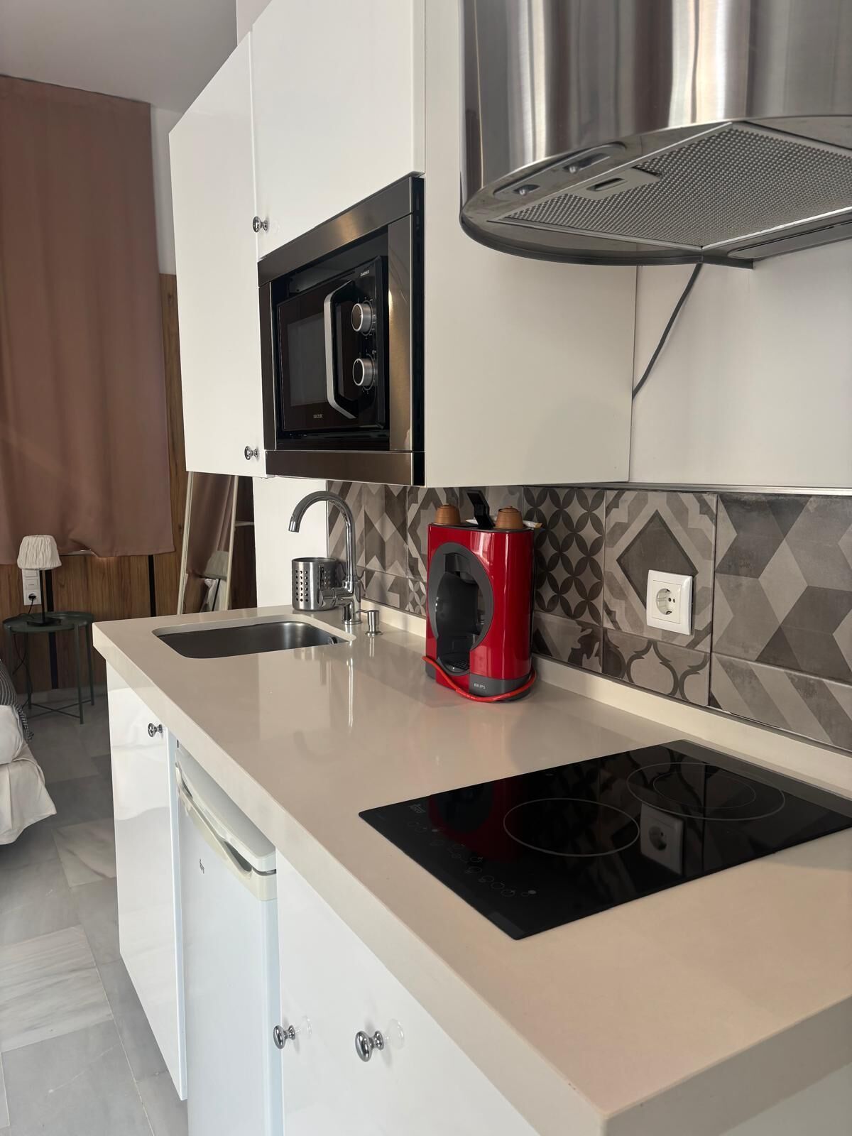 Una cocina moderna con microondas incorporado, una cafetera roja y una campana extractora de acero inoxidable.